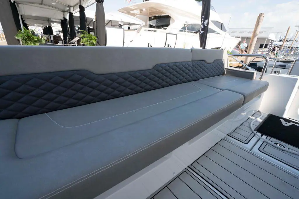 A modern grey and black upholstered boat seat with diamond stitching, set against a marina backdrop.